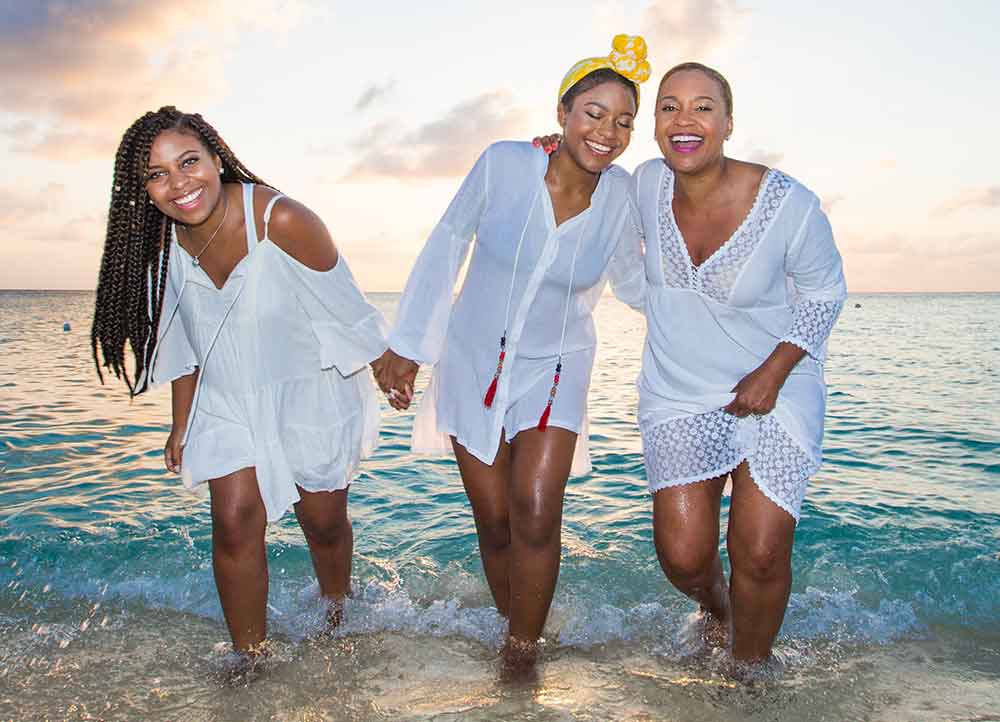 Three women in white dresses are walking on the beach.